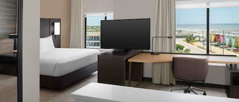 Ein Hotelzimmer mit Bett, Schreibtisch, Fernseher und Blick auf den Strand.