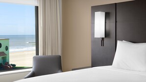 Une chambre d’hôtel avec un grand lit, une chaise, une table de chevet, une lampe et une vue sur la plage.