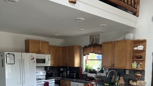A modern kitchen with wooden cabinets, a white refrigerator, a microwave, and a wooden island with bar stools.