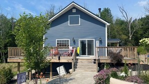 A two-story house with a deck, a covered porch, and a small garden area with flowers and plants.