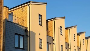 Eine Reihe moderner, zweistöckiger Wohngebäude mit einheitlicher Fassade, mit Balkonen und einem befestigten Eingangsbereich.