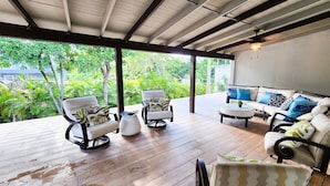 A covered outdoor seating area with wooden flooring, surrounded by lush greenery. - 6 guests, 4 min Walk to Private Beach, casino, bowling alley and much more ! 
 (Dorado)