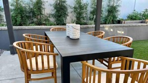 Een terras buiten met een rechthoekige tafel en zes houten stoelen met kussens.