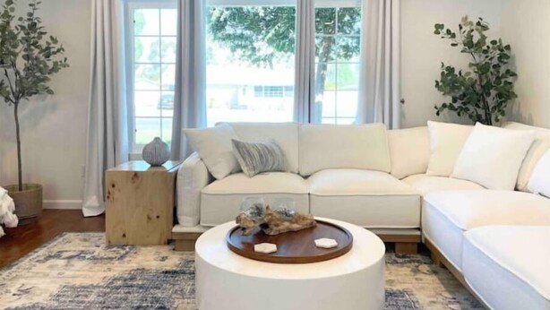 Een moderne woonkamer met een witte modulaire bank, een ronde salontafel en twee potplanten.