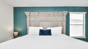 A bedroom with a large bed, a decorative headboard, a bedside lamp, and a window with blinds. - Amazing 4-BR Oasis With Pool & Backyard Bliss (Cypress)