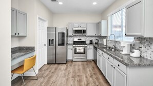 A modern kitchen with white cabinets, granite countertops, stainless steel appliances, and a yellow chair. - Amazing 4-BR Oasis With Pool & Backyard Bliss (Cypress)