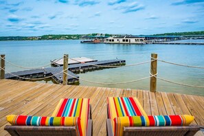 Une terrasse en bois avec deux chaises longues et une vue sur un lac où est amarré un bateau.