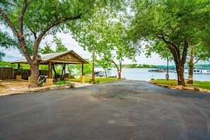 Un espace pique-nique abrité, équipé d’une table et de chaises, une allée pavée et une étendue d’eau où l’on aperçoit des bateaux au loin.
