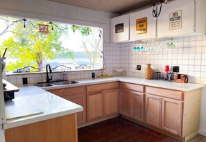 Une cuisine avec des meubles en bois, un plan de travail blanc et une fenêtre donnant sur un arbre.