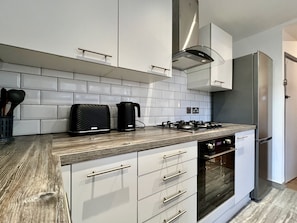 Uma cozinha moderna com armários brancos, geladeira de aço inoxidável, fogão a gás e forno embutido.