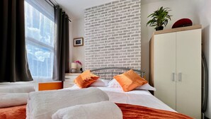 Une chambre d’hôtel avec un mur en briques, un lit avec une literie blanche et orange, une armoire et une fenêtre avec des rideaux.