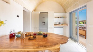 A modern kitchen with a wooden table set for breakfast, a built-in oven, and a sliding glass door leading to a patio. - 3517 Tenuta Venti Pamaridi by Perle di Puglia (Ostuni)