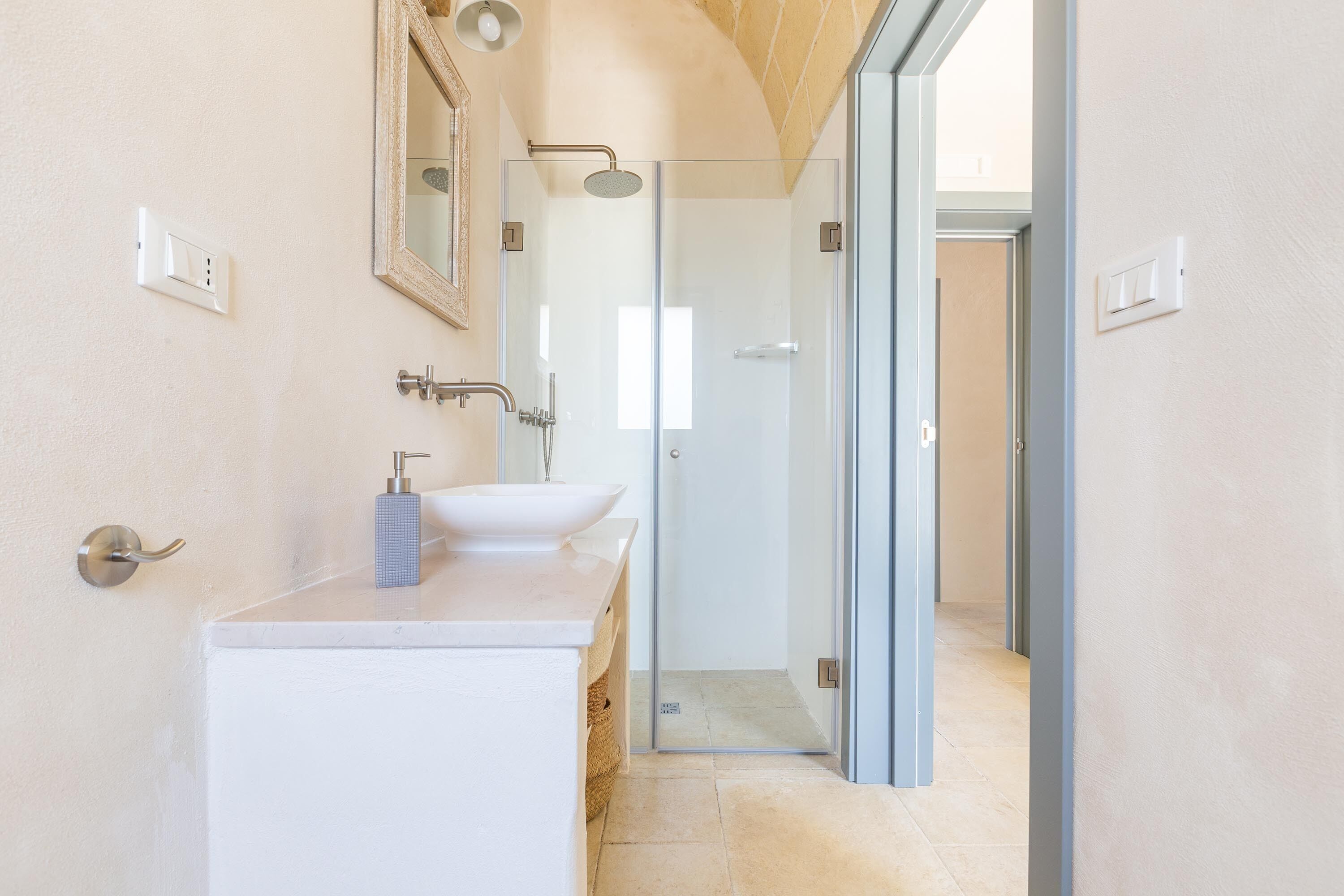 Een moderne badkamer met een witte wastafel, een douchecabine met glazen wanden en een deur naar een andere kamer.