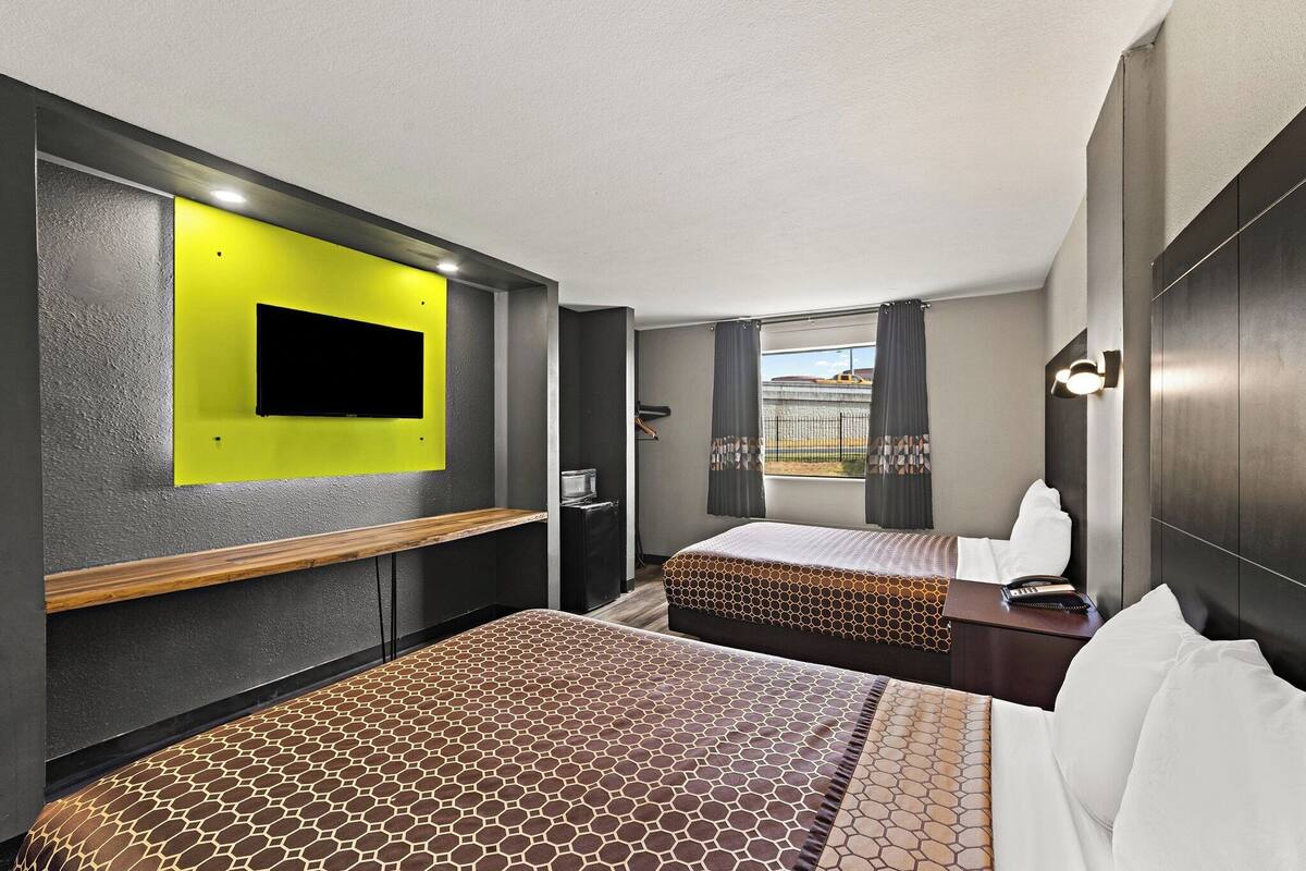 A hotel room with two beds, a TV mounted on the wall, a desk, and a window with curtains.