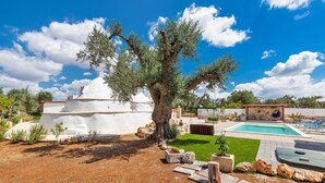 A pool area with a white building, a tree, and a clear blue sky.