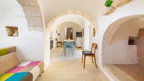 A narrow hallway with arches, a dining area with a table and chairs, and a sofa with a colorful cushion.
