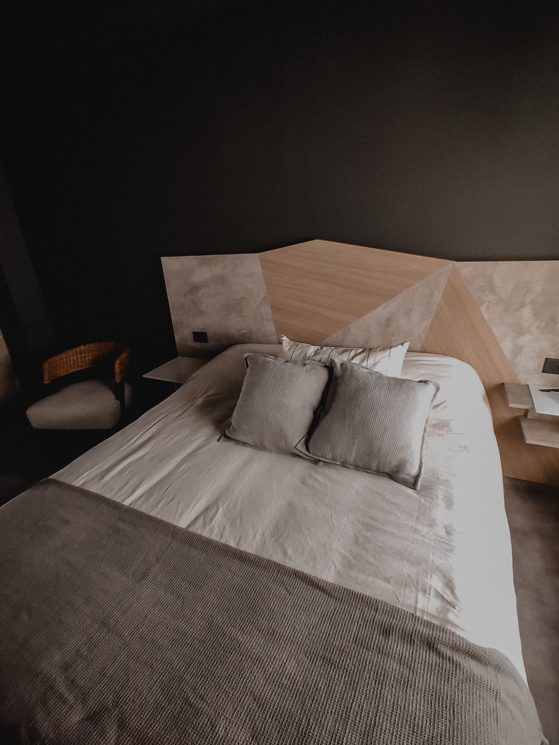 A modern bedroom with a large bed, two pillows, a wooden headboard, a nightstand, and a chair.