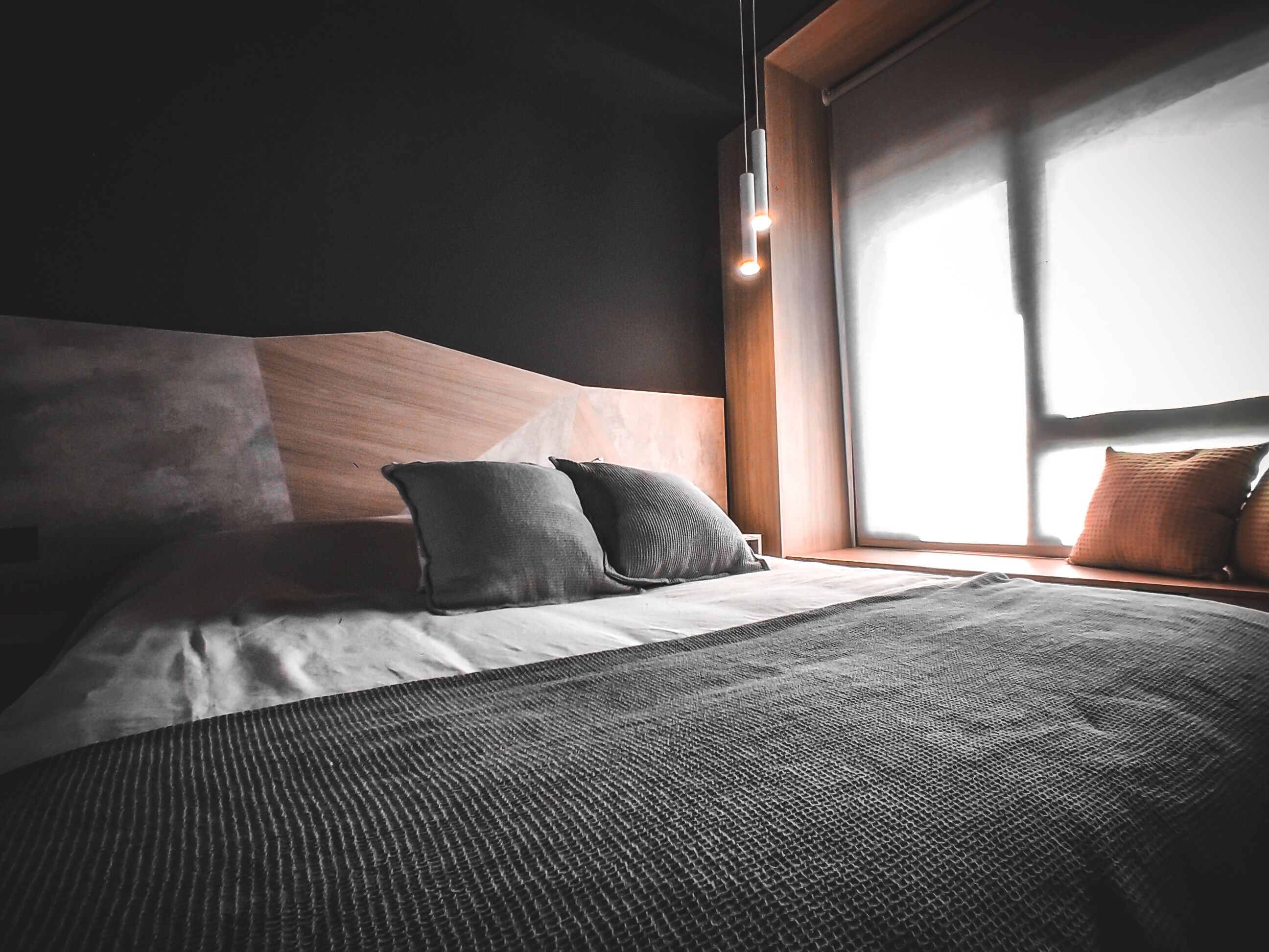 A modern bedroom with a large bed, two pillows, a textured blanket, and a window with blinds.