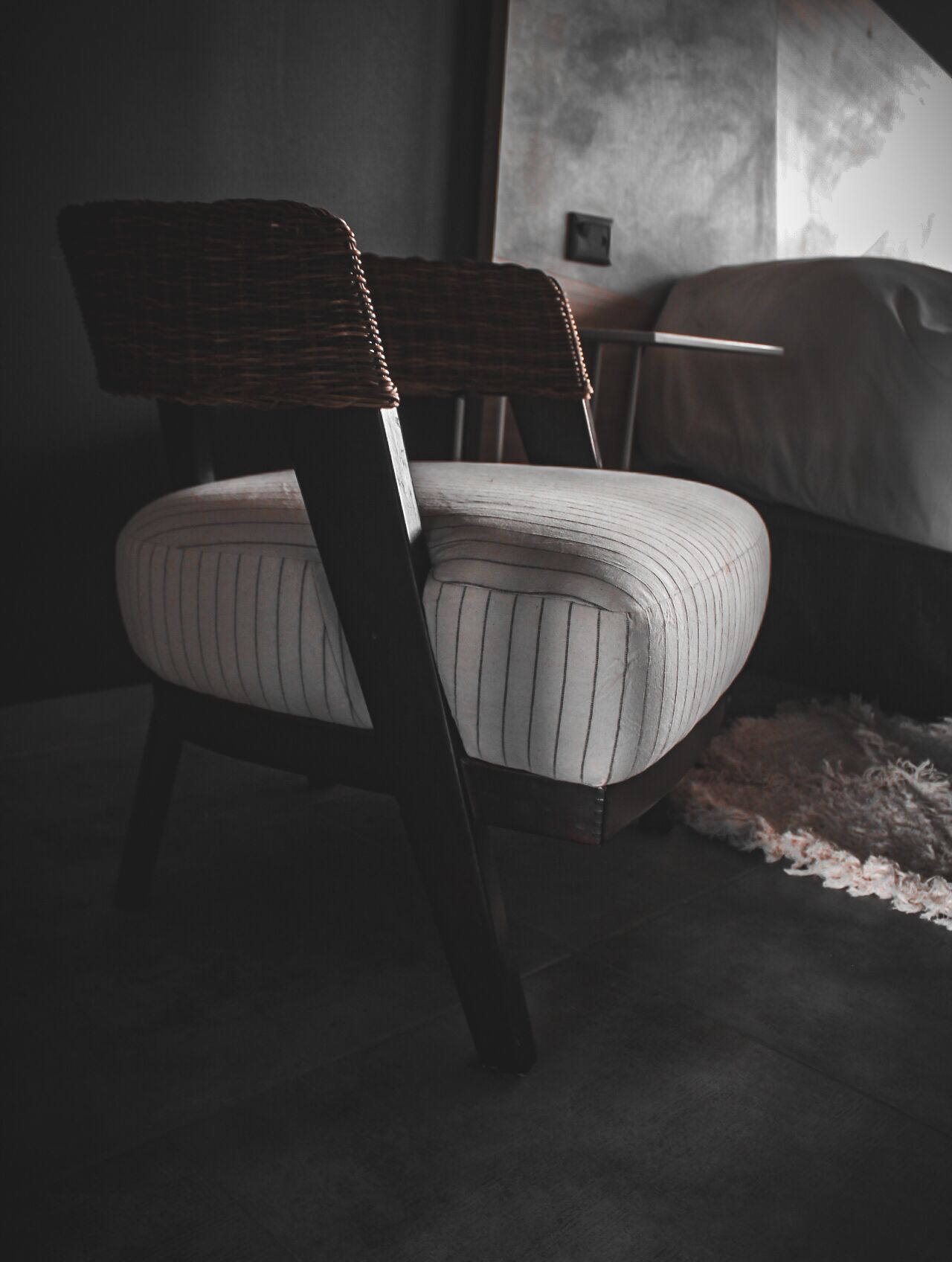 A chair with a woven backrest and striped upholstery in a dimly lit room with a textured wall and a visible power outlet.