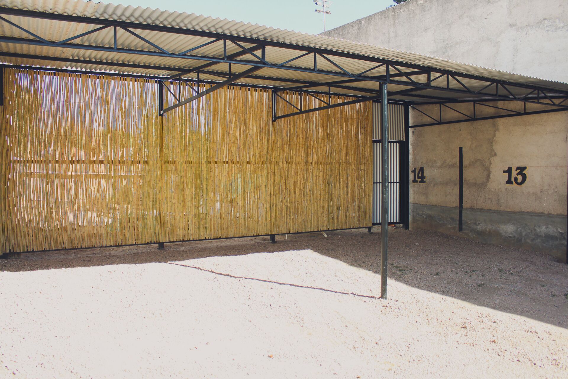 Un espacio al aire libre cubierto con pared de bambú y estructura de techo metálico.