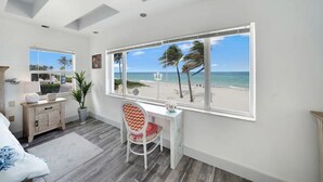 A bedroom with a large window overlooking a beach, a desk, and a chair. - *Magical Beachfront King Escape*

 (Hollywood)