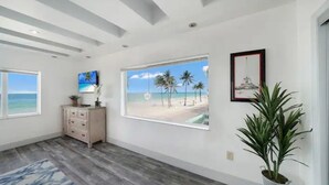 A spacious room with a large window offering a beach view, a wooden floor, a dresser, and a potted plant. - *Magical Beachfront King Escape*

 (Hollywood)