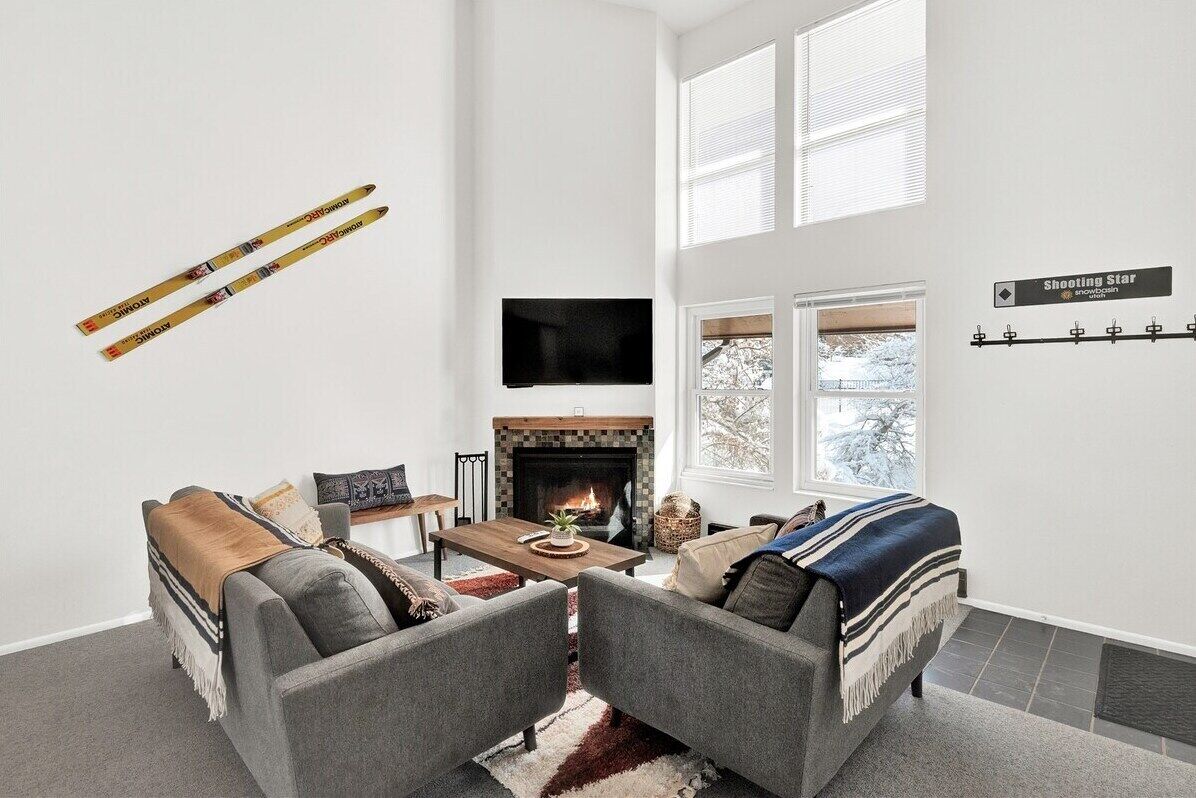 A modern living room with a fireplace, grey sofas, a coffee table, and a ski rack on the wall.