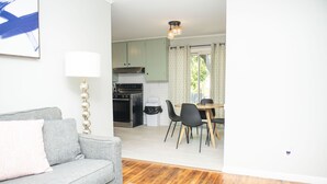 A living room with a grey sofa, a coffee table, and a lamp. There is a dining area with a table and chairs. The kitchen is visible in the background with a stove and cabinets. - Newly Remodeled 3 Bdrm 2 Bath near Expo Sq, TU, and Downtown (Tulsa)