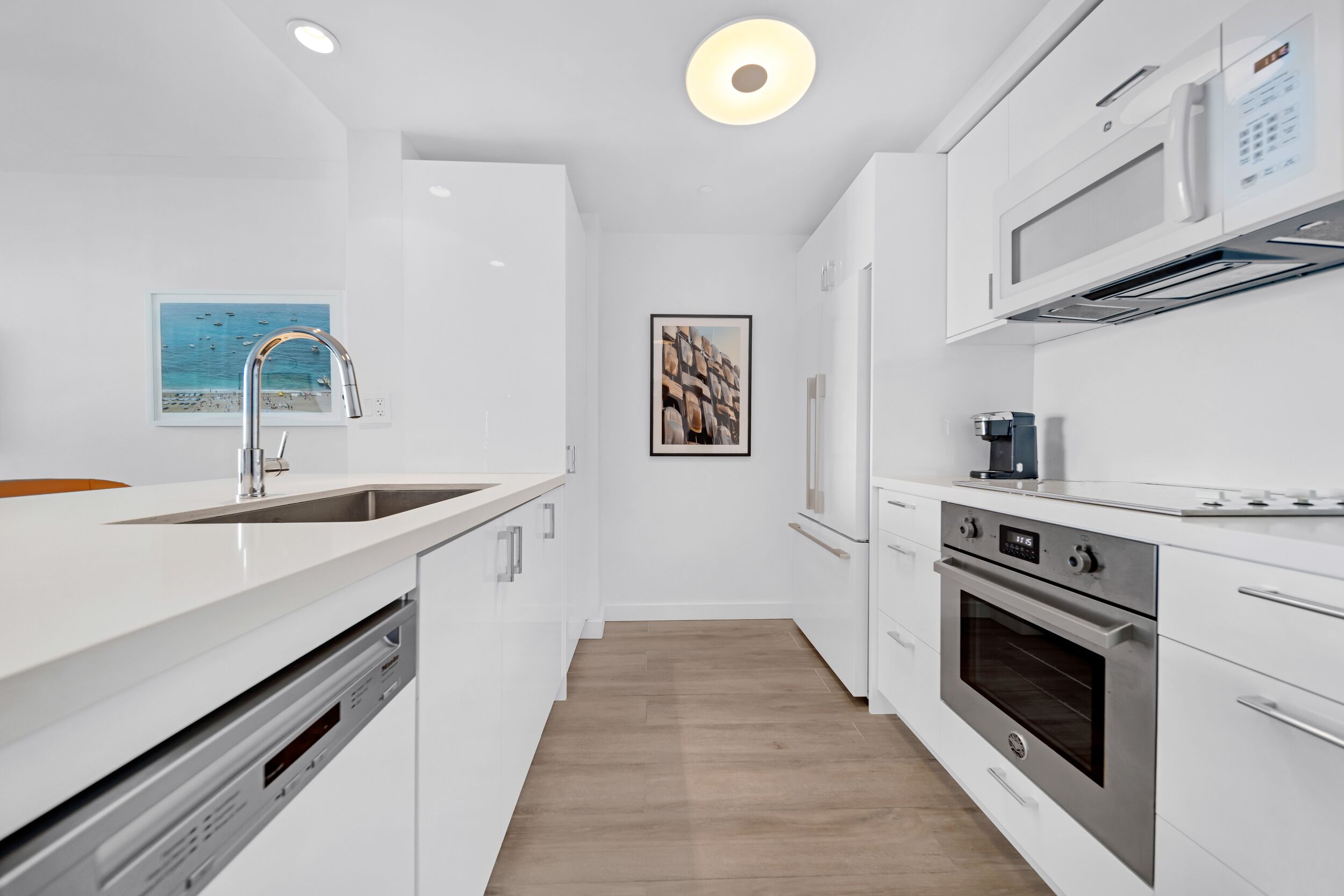 A modern kitchen with white cabinetry, stainless steel appliances, and a wooden floor.