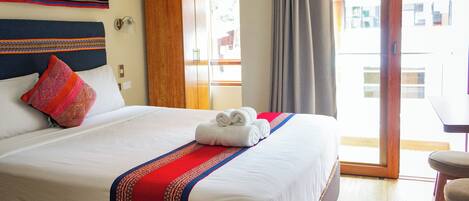 A hotel room with a large bed, a wooden wardrobe, a balcony with a table, and a view of the outside.