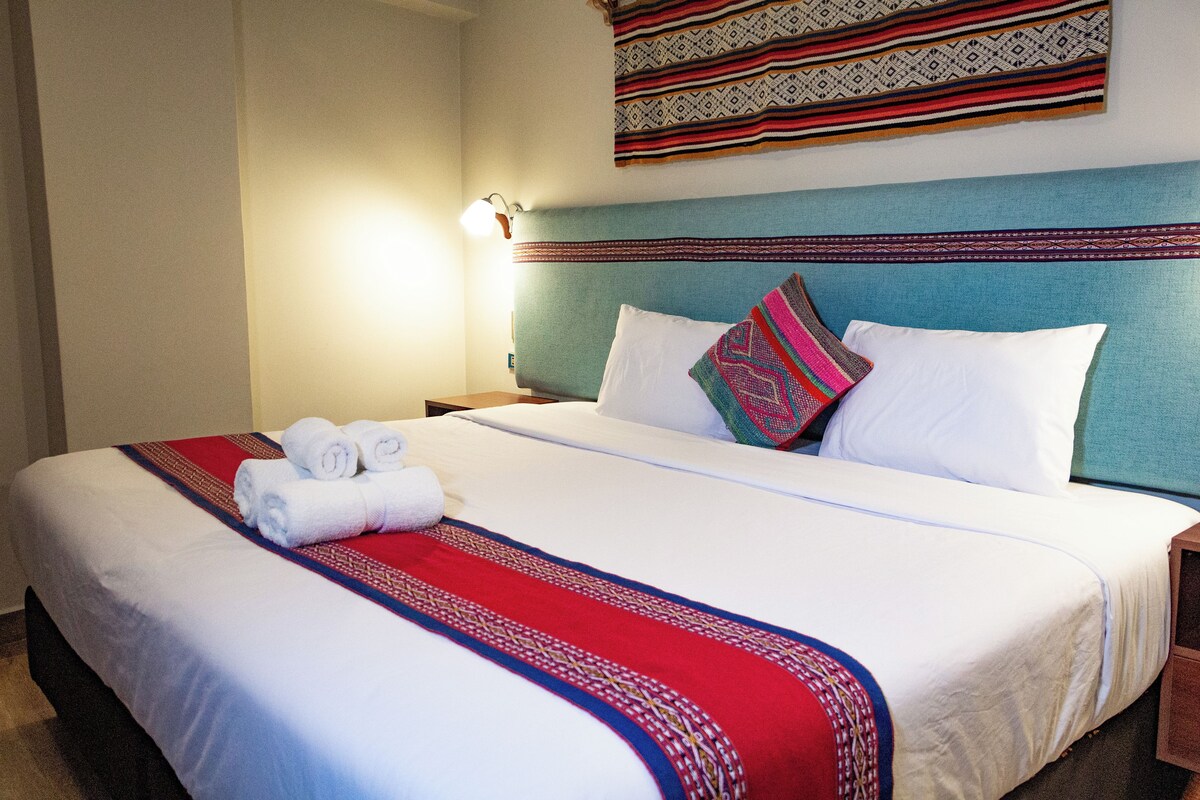 A neatly made bed with white linens and a red and blue patterned bedspread.