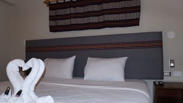 Habitación de hotel con cama, almohadas, cabecero, cortina instalada en la pared y mesita de noche con control remoto.