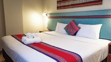 Cama bem arrumada com lençóis brancos e um edredom estampado em vermelho e azul.