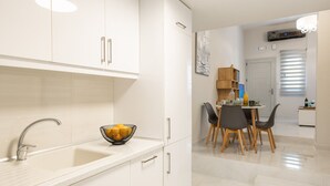 A modern kitchen with white cabinetry, a sink, and a dining area with a table and chairs. - Corfu Luxury Loft by Corfuescapes (Corfu)