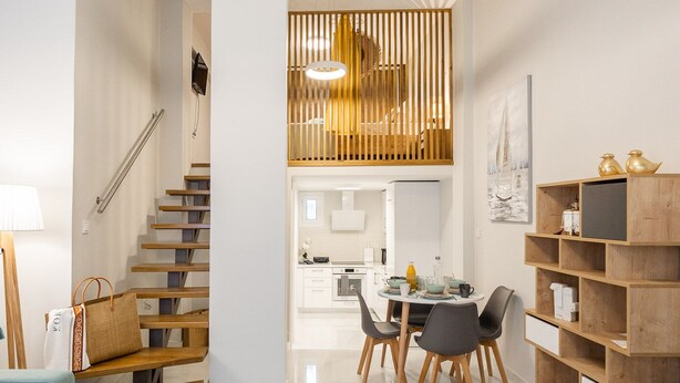 A modern living room with a wooden staircase, a dining area with a table and chairs, and a bookshelf. - Corfu Luxury Loft by Corfuescapes (Corfu)