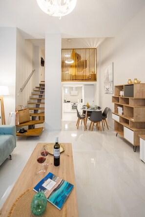 A modern living room with a wooden staircase, a dining area with a table and chairs, and a bookshelf. - Corfu Luxury Loft by Corfuescapes (Corfu)
