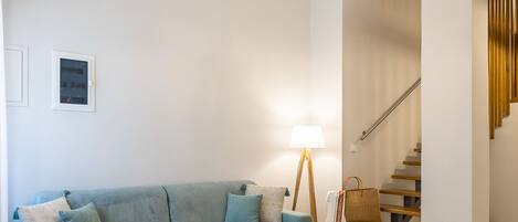 A modern living room with a sofa, a coffee table, a lamp, and a staircase.