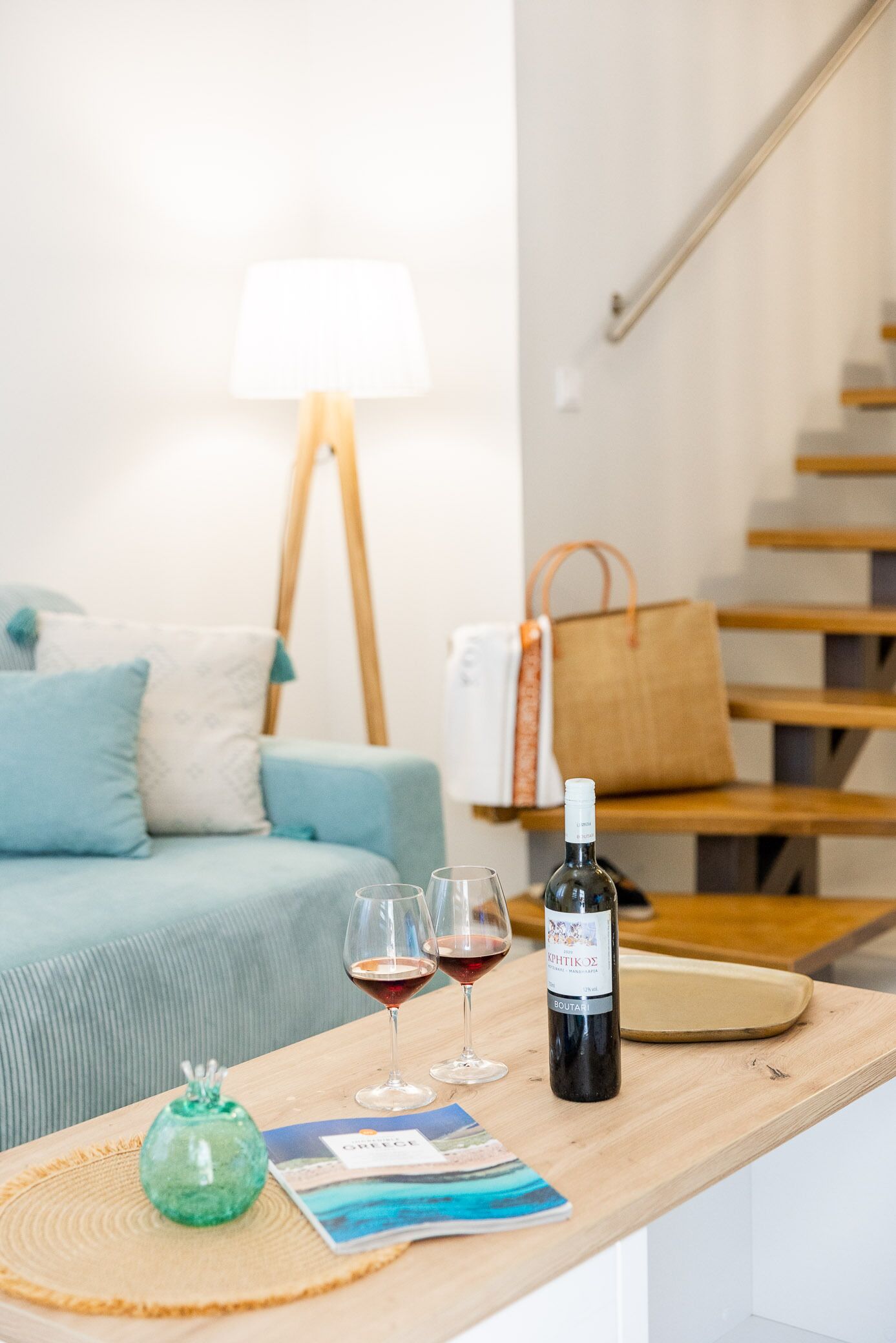 A wooden table with a bottle of wine, two wine glasses, and a magazine.