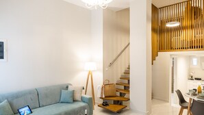 A modern living room with a sofa, coffee table, and a staircase leading to a dining area. - Corfu Luxury Loft by Corfuescapes (Corfu)