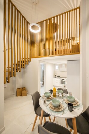 Een eetruimte met een ronde tafel gedekt voor vier personen, omringd door stoelen. Een trap met houten leuningen leidt naar een hoger niveau.