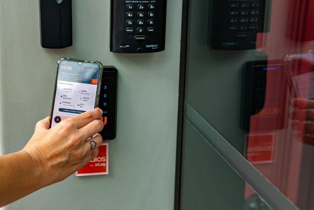 A hand holding a smartphone with a payment app interface, a keypad, and a sign with "xat" on it.