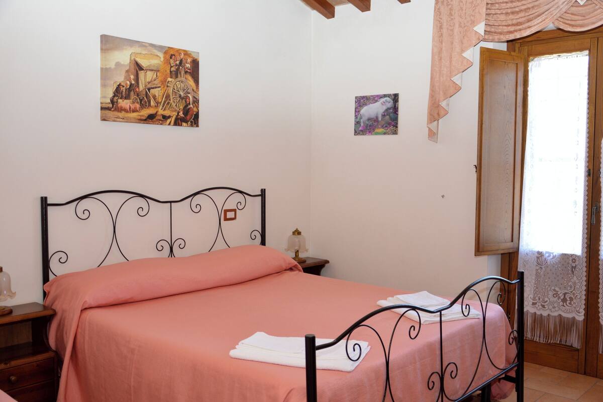 Un dormitorio con cama, mesita de noche, lámpara y un cuadro en la pared.