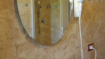 A bathroom with a white sink, a green soap dispenser, a handheld hair dryer, and a shower with a glass door.