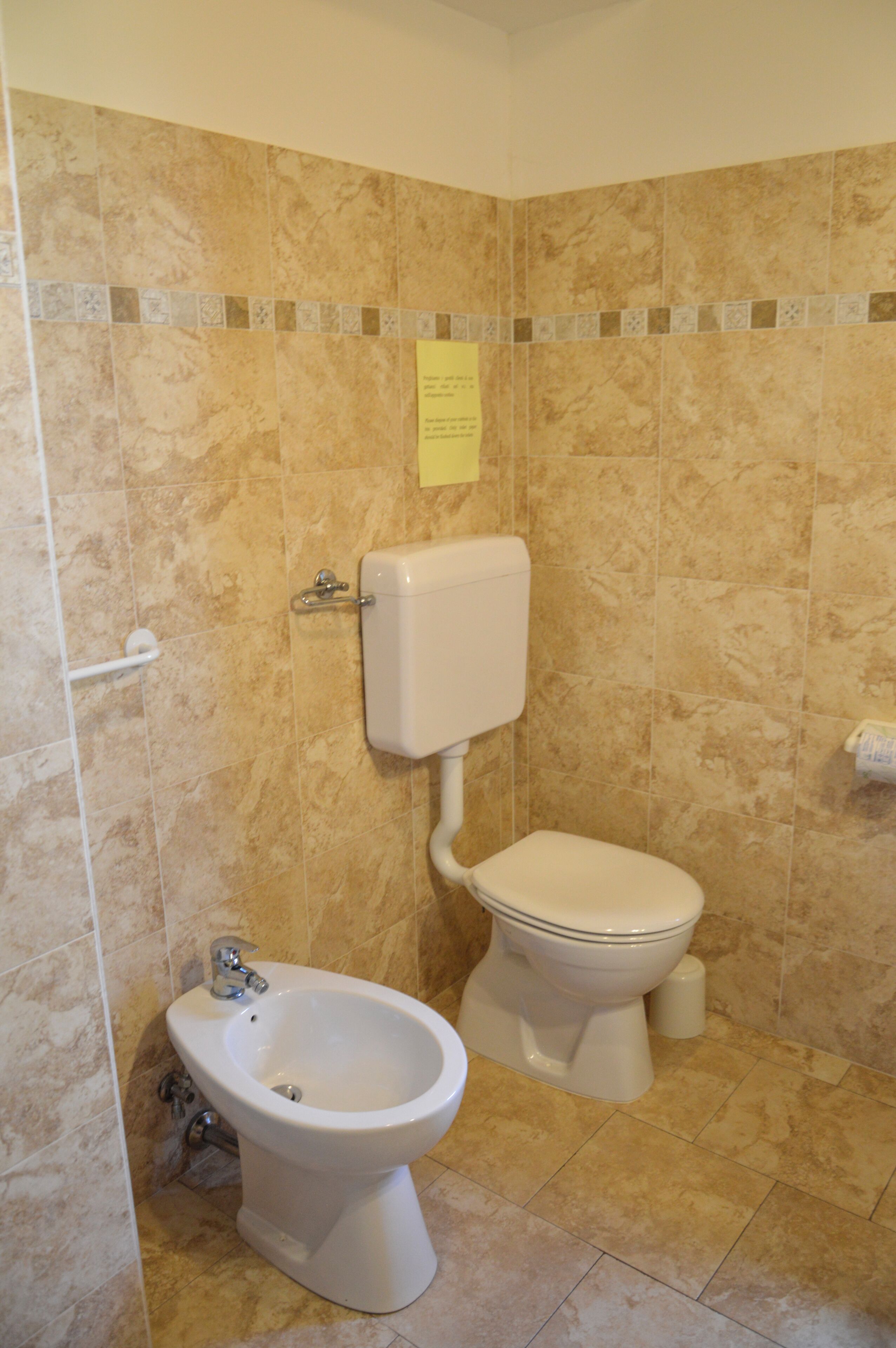 A bathroom with a bidet, toilet, and a wall-mounted paper towel dispenser.