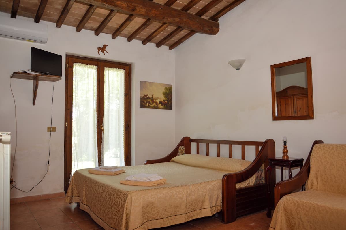 Un dormitorio con cama de madera, una silla, televisión montada en la pared y ventana con cortinas.