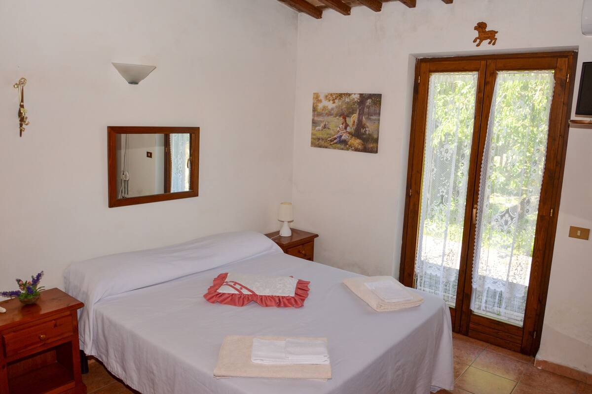Un dormitorio con cama, mesita de noche, espejo, un cuadro y una puerta con vistas.