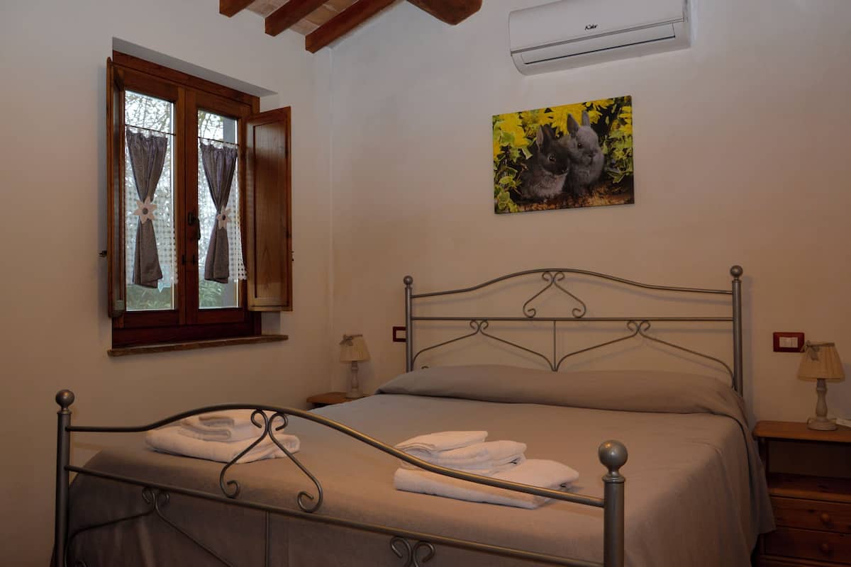 Un dormitorio con estructura metálica para la cama, una ventana con cortinas, un aire acondicionado instalado en la pared y un cuadro de un conejo.