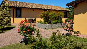 A yellow building with a tiled roof, a paved garden area with roses, and a stone bench. - La Fraschetta (Bolsena)