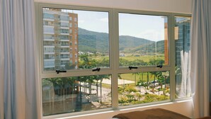 A bedroom with a large window offering a view of a building and a green landscape. - Apartment 01 double room (Palhoça)