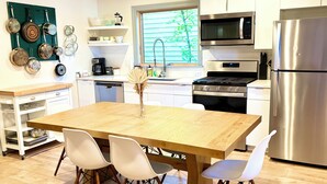 Une cuisine moderne avec des meubles blancs, des appareils en acier inoxydable et une table à manger en bois, accompagnée de quatre chaises.